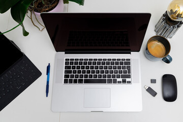 flatlay of open laptop with mug, mouse, usb drive, pen and tablet