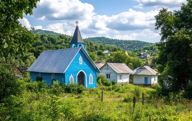 Fototapeta premium Photo of a blue church in the Carpathian Mountains, surrounded by greenery and trees, on top of a hill in a Ukrainian village with white wooden houses, with a nature landscape background