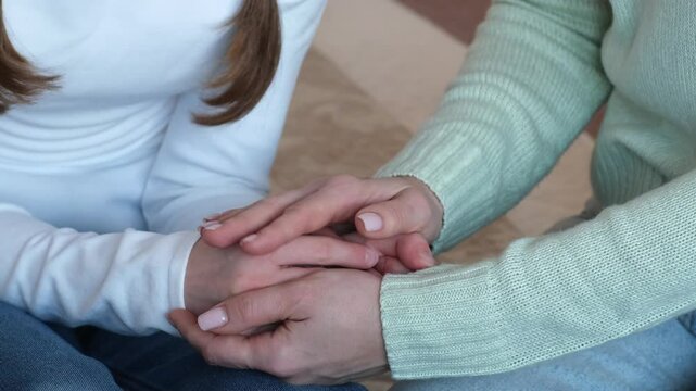 Mother holding hands of kid girl, supporting and protecting her daughter at home. Child and mom are together. Parent helping to solve problem. Concept of family love and support