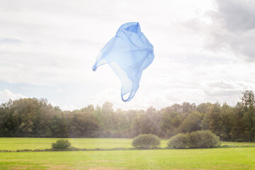 environmental plastic waste pollution in nature: disposable plastic bag over idyllic countryside
