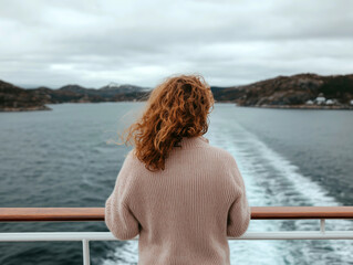 Fototapeta premium Peaceful moment on a ferry: Woman admiring misty fjords with serene water and forested mountains