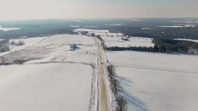 Car Driving On A Snow Covered Road In A Rural Farm Landscape During Winter, Aerial Tracking Shot.
