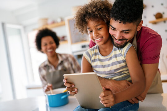 Happy african family having fun with device at home, using digital tablet looking at screen together