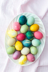 Multi-colored Easter eggs in an oval dish on a pink tablecloth, top view, Happy Easter holiday