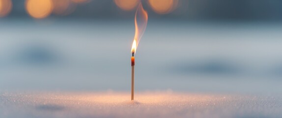Single glowing matchstick burning with a small flame on a white surface during evening hours.