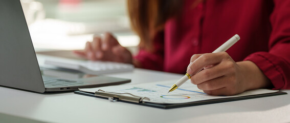Businesswoman working with financial data, using calculator and analyzing charts on clipboard,...