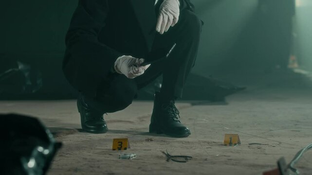 Tilt up low-key shot of young Caucasian female forensic expert in gloves examining evidence at crime scene, analyzing cracks of broken smartphone together with joining Black male colleague