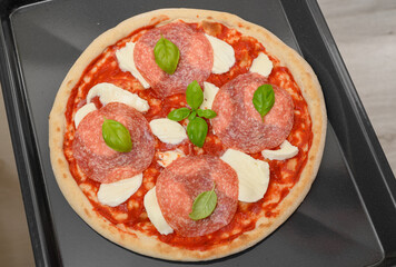 Pizza z salami mozarellą, sosem pomidorowym i bazylią na blaszce do pieczenia 