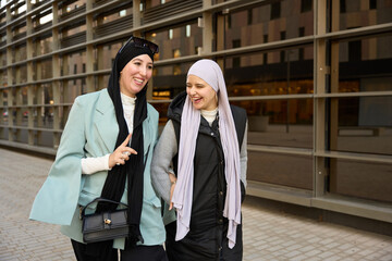 Two smiling muslim businesswomen walking and talking on city street