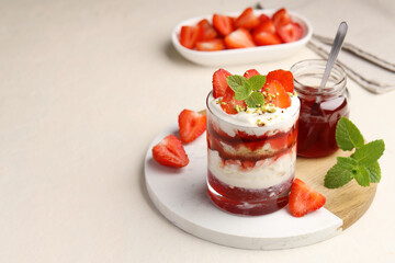 Tasty trifle dessert. Strawberries, sponge cake and whipped cream in glass on beige table, space...