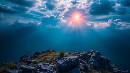 Majestic mountain peak showcasing a breathtaking sunset with sun rays piercing through dramatic clouds and a rocky foreground.