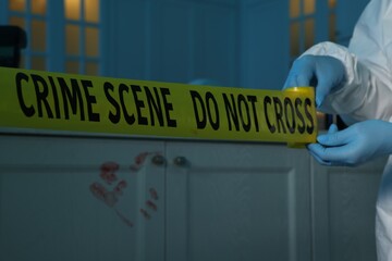 Forensic expert blocking way to crime scene with yellow tape indoors, closeup