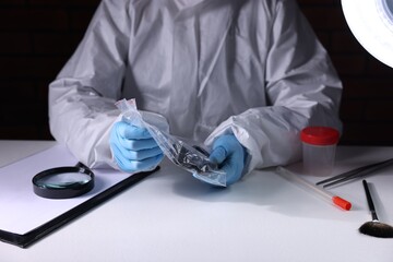 Forensic expert examining evidence in plastic bag at table indoors, closeup