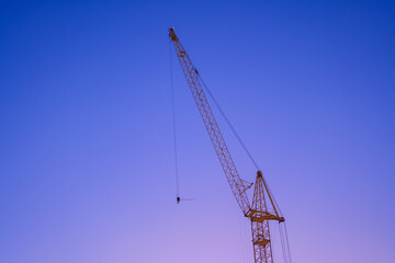 Silhouette of a construction crane against the background of a beautiful sky in pink and blue colors. Blue hour. minimalism. Clear gradient sky.