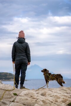 Back view of woman and dog on top of a cliff looking at Mount Athos