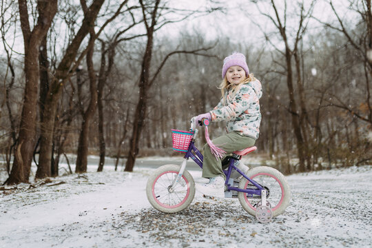 Cheerful child riding bicycle in driveway on snow day