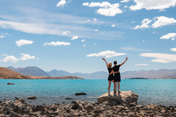 Two hikers enjoying the view of Lake Tekapo on a summer day with blue sky and some white clouds (Tekapo, South Island, New Zealand)