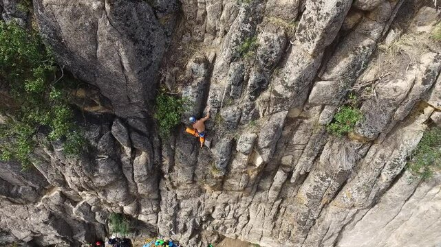 Imagen a&eacute;rea de escalador subiendo por una pared de roca con un grupo de escaladores abajo en el suelo
