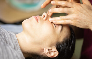 man massages a woman's face. The woman is relaxed and enjoying the massage. The man is using his hands to apply pressure to the woman's face