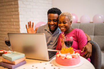 Happy young couple celebrating woman's birthday at home. They are having video call with family.