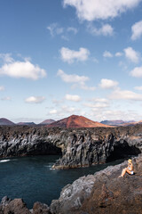 Los Hervideros coastline view with a woman relaxing on rocky terrain by the sea