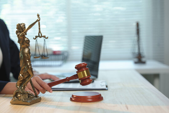 Lawyer is holding a gavel in courtroom with justice statue and laptop in background, representing legal system, justice, and law enforcement