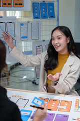 Asian female web designer pointing at ux ui smartphone templates hanging on a grid explaining...