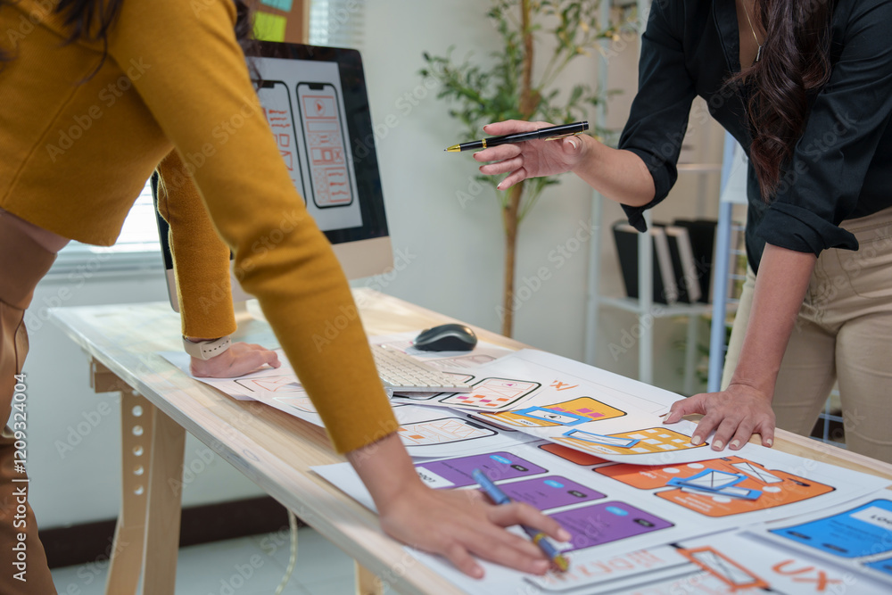 Poster two female ux designers are collaborating on wireframes for a mobile app, meticulously reviewing and