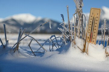 Wooden thermometer measuring freezing temperatures in a snowy landscape with ice-covered grass and...