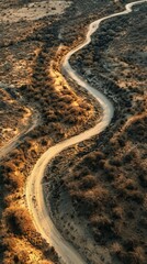 Obraz premium A winding dirt road meanders through an arid landscape. The sunlight casts shadows on the textured terrain. Explore the beauty of nature in this serene scene. Generative AI