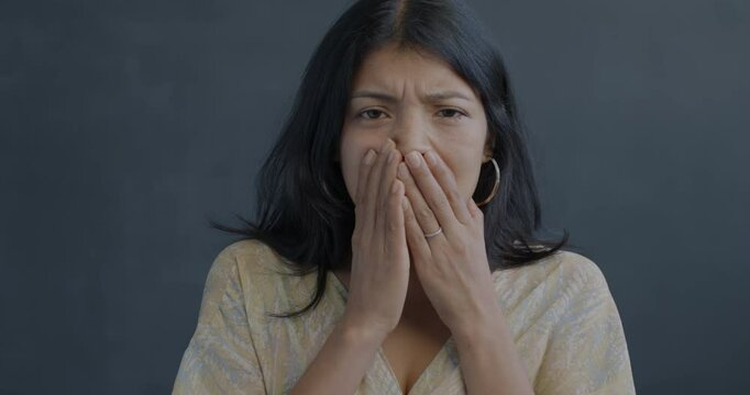 Portrait of shocked Hispanic lady shaking head covering mouth on black background. Negative emotion and bad news concept.
