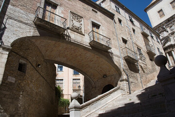 A charming stone archway connects vintage buildings in a historic setting, showcasing intricate architectural details and the beauty of old-world craftsmanship in Girona Catalonia Spain