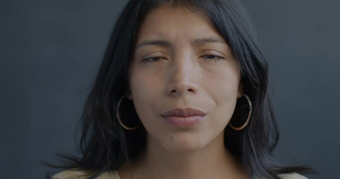 Close-up portrait of unhappy Hispanic lady looking at camera on black background. Negative emotion and miserable person concept.