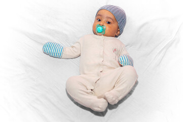 Portrait of a three-month-old baby lying down with a winter romper, hat, gloves, and a pacifier in...