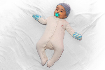 Portrait of a three-month-old baby lying down with a winter romper, hat, gloves, and a pacifier in...