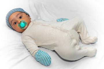Portrait of a three-month-old baby lying down with a winter romper, hat, gloves, and a pacifier in...