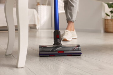 Woman cleaning floor with cordless vacuum cleaner at home, closeup