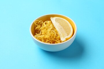 Lemon zest and piece of fresh fruit on light blue background, closeup