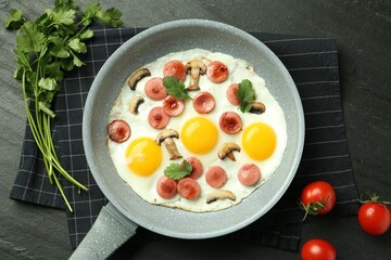 Tasty fried eggs with cut sausages and mushrooms served on black table, flat lay
