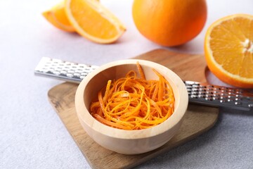 Fresh orange zest in bowl, fruits and grater on grey textured table, closeup