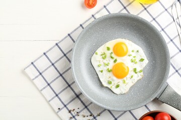 Tasty fried eggs with green onion in frying pan on white wooden table, top view. Space for text