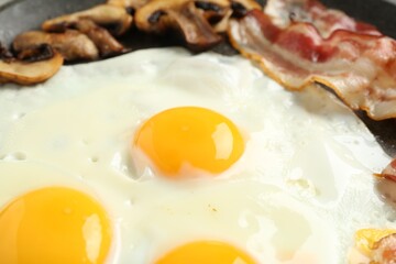 Tasty fried eggs with bacon and mushrooms in frying pan, closeup