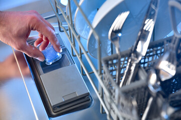 Hand inserting a dishwasher detergent tablet into the door compartment