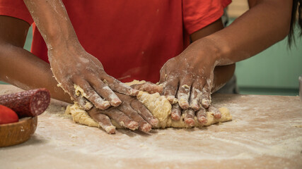 African American mother and little son preparing healthy meal, mom helping son kneading dough on the wooden table, close up shot.