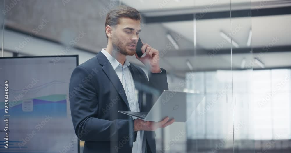 Aufkleber young manager having a call with a client as he stands in an office, holding laptop computer and tal