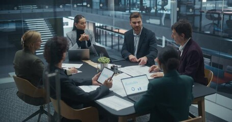 Colleagues Discussing Business Opportunities in a Glass Conference Room, Using Laptops, Tablets and Printed Documents. They Share Knowledge, Exchange Practices, Build Strong Working Relationships