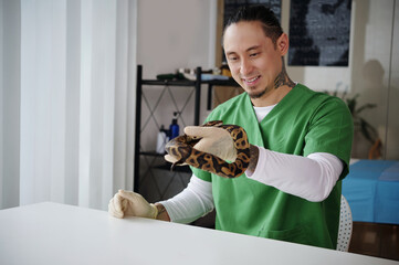 Veterinary professional handling snake with care in clinic room. Smiling calmly while wearing green...