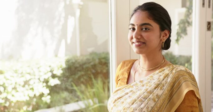 Smiling Indian woman in traditional Indian sari standing by window, looking confident, copy space