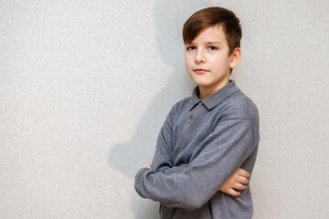 a ten year old boy in a gray sweater stands against a wall with his arms crossed over his chest