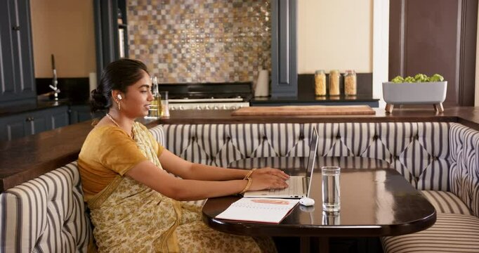 Working from home, Indian woman in saree using laptop and earbuds in kitchen, copy space